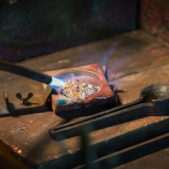 goldsmith melting gold and silver granules in a  crucible with a gas flame from a blowtorch in a jewelry, copy space, selected focus, narrow depth of field