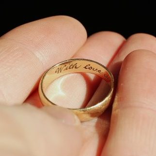 A man holds a wedding ring engraved "with love"