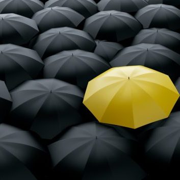 Different and unique yellow umbrella in a row of black ones